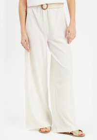 Pantalones de pierna ancha en color crema, elaborados con una tela texturizada, que cuentan con una cintura elástica y un cinturón trenzado. Combinados con sandalias planas.