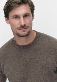 Ruskea neulepaita, jossa on pyöreä kaula-aukko ja resorit, ominaisuutena pehmeä yksityiskohta ja tasainen väri kauttaaltaan.