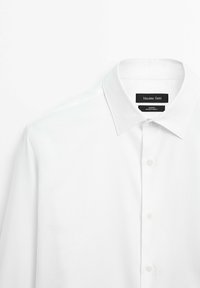 Weißes Hemd mit klassischem Kragen, Knopfleiste und strukturierter Baumwolle. Markenlabel sichtbar unter dem Kragen.