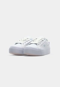 Baskets blanches avec une tige en texture lisse, design à lacets et tige basse. Présente un accent bleu subtil et une semelle blanche surélevée.