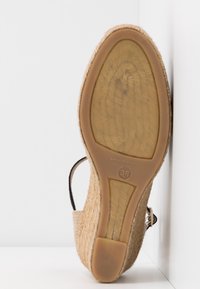 Chaussure compensée espadrille en tissu beige tissé, semelle en caoutchouc marquée "Made in Spain" et taille 38, positionnée côté semelle contre une surface blanche.