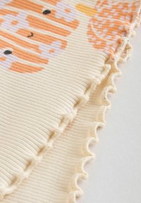 Pehmeä ribbikankaasta valmistettu viltti, jossa on oransseja ja pastellisävyisiä eläinkuvioita, sekä taitettu reuna. Pääväri on kerma, ja siinä on tekstuuria kauttaaltaan.