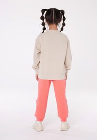 Light beige sweatshirt with a relaxed fit and crew neck, paired with coral sweatpants, featuring ribbed cuffs and white sneakers.
