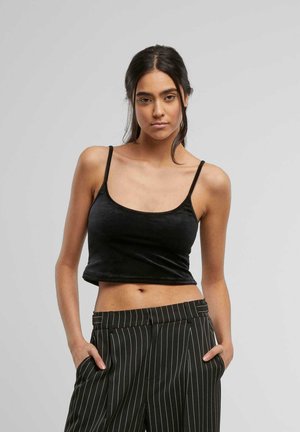 Top scurt negru din catifea moale, cu bretele subțiri și decolteu rotund, purtat cu pantaloni cu dungi negre și albe.
