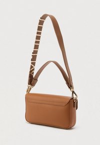 Brązowa skórzana torebka na ramię z dwoma paskami, jednym z złotym elementem i ozdobionym inicjałami, na jasnym tle.