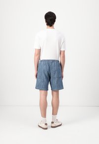 Shorts de mezclilla con un patrón texturizado azul, cinturilla elástica, bolsillo lateral y corte recto. Combinados con una camiseta blanca sencilla y zapatillas.