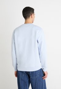 Sudadera azul clara hecha de un tejido suave, con un cuello redondo acanalado y puños, combinada con jeans azul rayados.