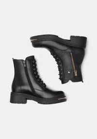 Zwarte leren enkelboots met een chunky hak, voorzien van een zijrits en decoratieve kantdetails. Textuurafwerking en gouden accenten.