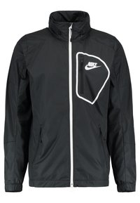 Svart Nike vindjacka med dragkedja framtill, hög krage, vit dragkedja och en framträdande bröstficka med Nike-logotypen.