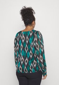Langärmlige Bluse mit schwarzem Grund und grünen sowie braunen geometrischen Mustern. Faltentextur mit rundem Halsausschnitt und enganliegenden Manschetten.