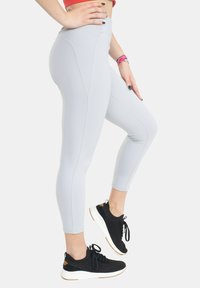 Leggings gris clair avec une taille haute, des coutures plates et un design ajusté ; accompagnés de chaussures de sport noires avec une semelle blanche.