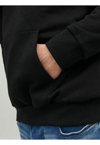 Zwarte sweatshirt met een buidelzak, geribbelde manchetten en zoom. Zachte textuur, casual pasvorm, gecombineerd met lichtblauwe jeans.
