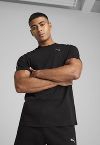 Svart bomulls-t-shirt med korta ärmar, med en liten vit Puma-logotyp på bröstet och en enfärgad design.