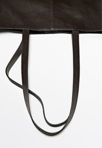 Zwarte leren tote bag met twee lange handvatten, voorzien van een gladde, gestructureerde afwerking en strakke randen, ontworpen voor een minimalistische esthetiek.