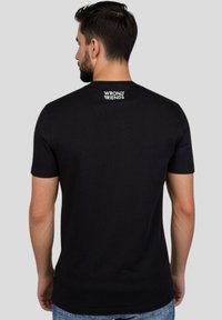 Černé tričko s krátkým rukávem a kulatým výstřihem. Na horní části zad se nachází bílé logo "WRONG FRIENDS". Hladká textura, přiléhavý střih.