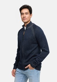 Marine blauwe zip-up trui met een hoge kraag, textuur gebreide stof en houten ritslip. Kenmerkt zich door geribbelde manchetten en subtiele details.