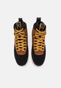 Höga sneakers med ett svart nätöverdel, bruna läderaccenter och gula snören. Har en texturerad sula och en dragflik på hälen.