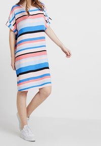 Robe rayée en rose pastel, bleu et noir; coupe décontractée avec des manches courtes; tissu doux; longueur au genou; portée avec des baskets blanches.