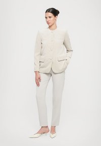 Giacca in corduroy beige chiaro con scollo rotondo e tre bottoni, abbinata a pantaloni grigi chiari su misura e mule crema a punta.