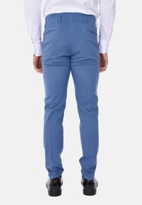 Pantaloni in cotone blu con una vestibilità slim, dotati di due tasche posteriori e una texture liscia. Abbinati a scarpe nere lucide.