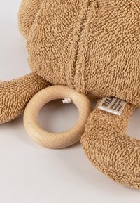 Soft, beige plush toy with textured fabric, featuring a wooden ring and tag. Round, smooth ring accentuates the design.