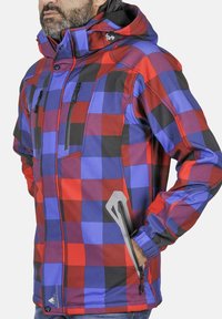 Veste à carreaux rouge, bleu et noir avec une capuche. Elle dispose de poches zippées, de poignets ajustables et d'un matériau résistant à l'eau.