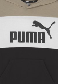 Sudadera Puma con un diseño a bloques de color en beige, blanco y negro. Incluye un bolsillo tipo canguro y un logo en negro. Textura de tela suave.