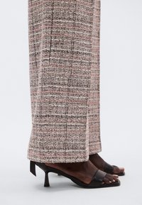 Textured, high-waisted trousers in pink, black, and cream with a check pattern, paired with black heeled sandals featuring a minimal strap design.