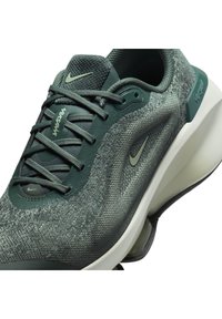 Las deportivas Nike verdes cuentan con una parte superior de malla texturizada, suela lisa y curva, y un branding sutil. Incluyen cordones oscuros y detalles en los ojales.