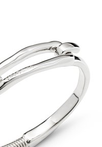 Pulsera de plata con un diseño suave y redondeado. Presenta un detalle en espiral y un sutil grabado de la marca, enfatizando un acabado pulido.