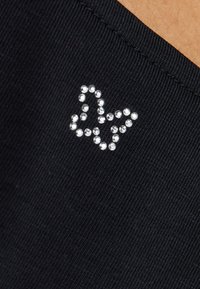 Tissu noir avec une texture lisse, présentant un motif de papillon orné de cristaux dans le coin inférieur.