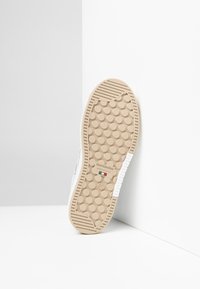 Shoe outsole with a light brown rubber material, featuring a textured circular pattern, a white accent, and branding on the heel.