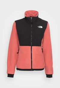 Różowa polarowa kurtka z czarnymi ramionami, wysokim kołnierzem, pełnym zapięciem na zamek z przodu, kieszeniami bocznymi oraz logo The North Face na piersi.
