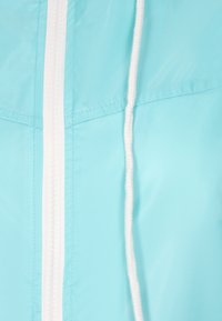 Lichtblauwe windbreaker met een witte rits en verstelbaar koord. Gladde, lichte stof met gestikte naden en een eenvoudig ontwerp.