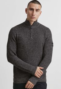 Mørkegrå, strikket pullover med kvart-lynl�ås, ribbet tekstur og huller til tommelfingrene i ærmerne. Har et logo på ærmet.