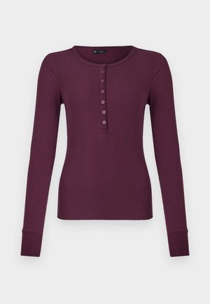 Chemise henley à manches longues en tricot côtelé dans une teinte prune foncé, avec sept boutons et des manches à poignets.