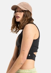 Sort cropped tank top i tekstureret stof, med sidesnit og trykknapdetaljer. En beigefarvet kasket med broderet tekst fuldender looket.