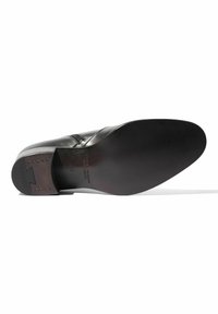 Zapato de cuero negro con parte superior lisa y punta redondeada. El tacón de madera marrón presenta pequeños tachuelas metálicas cerca de la parte trasera. Suela plana.