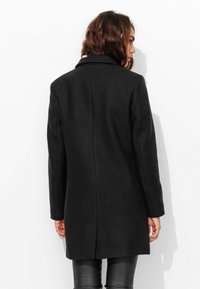 Manteau noir en mélange de laine avec un design ajusté, des manches longues et un col à revers. Texture lisse avec une silhouette nette et structurée.