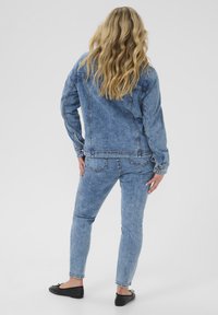 Chaqueta de mezclilla azul claro y jeans a juego, ambos con un diseño clásico y detalles de costura. La persona está de espaldas, revelando el ajuste de la ropa.