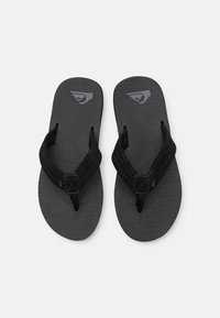 Tongs noires avec semelle texturée, brides en tissu et logo proéminent sur le dessus. Le détail de la couture sur les brides ajoute du contraste.