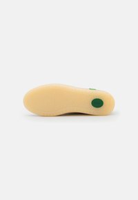 Semelle de sneaker en caoutchouc beige avec un motif de tread texturé, mettant en avant un accent logo vert. Bords lisses et arrondis et design flexible.