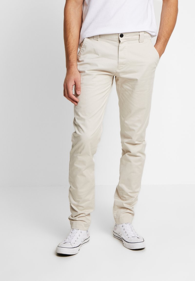 Beige bomullschinos med rak passform, med en knappstängning och sidofickor, i kombination med vita snörskor. Slät textur.