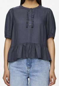 Femme portant un haut à manches courtes bleu marine avec une patte de boutonnage à volants à l'avant et un ourlet peplum, associé à un jean en denim bleu clair.