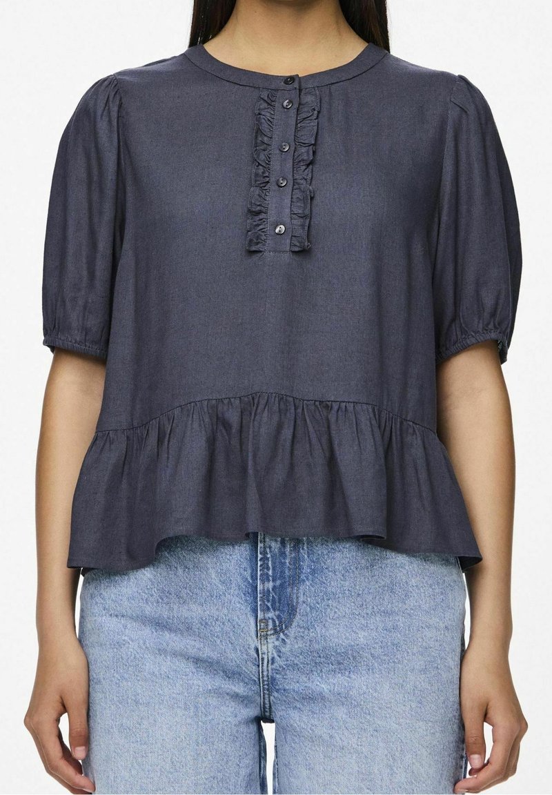 Femme portant un haut à manches courtes bleu marine avec une patte de boutonnage à volants à l'avant et un ourlet peplum, associé à un jean en denim bleu clair.