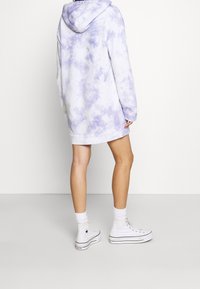 Mikina s kapucí v fialovém tie-dye vzoru, oversized střih, s elastickými manžetami a lemem, doplněná bílými teniskami s vysokým střih a bílými ponožkami.