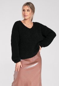 Schwarzer, flauschiger Pullover mit weitem Ausschnitt und langen Ärmeln, kombiniert mit einem glänzenden, hellrosa Satinrock. Weiche Textur und lässige Passform.