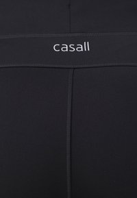 Černé legíny vyrobené z elastického materiálu s hladkou texturou, se širokým elastickým pasem s bílým logem "casall".