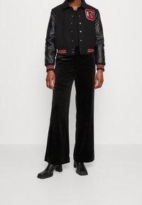 Svart varsityjacka med läderärmar, röda och vita detaljer och logotyp. Matchas med högmidjade svarta velourflaredbyxor och stövlar.