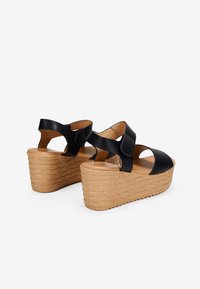 Sandales compensées en cuir noir avec un bout ouvert, mettant en valeur une semelle en liège texturée. Comprend une sangle ajustable et des découpes sur les côtés.